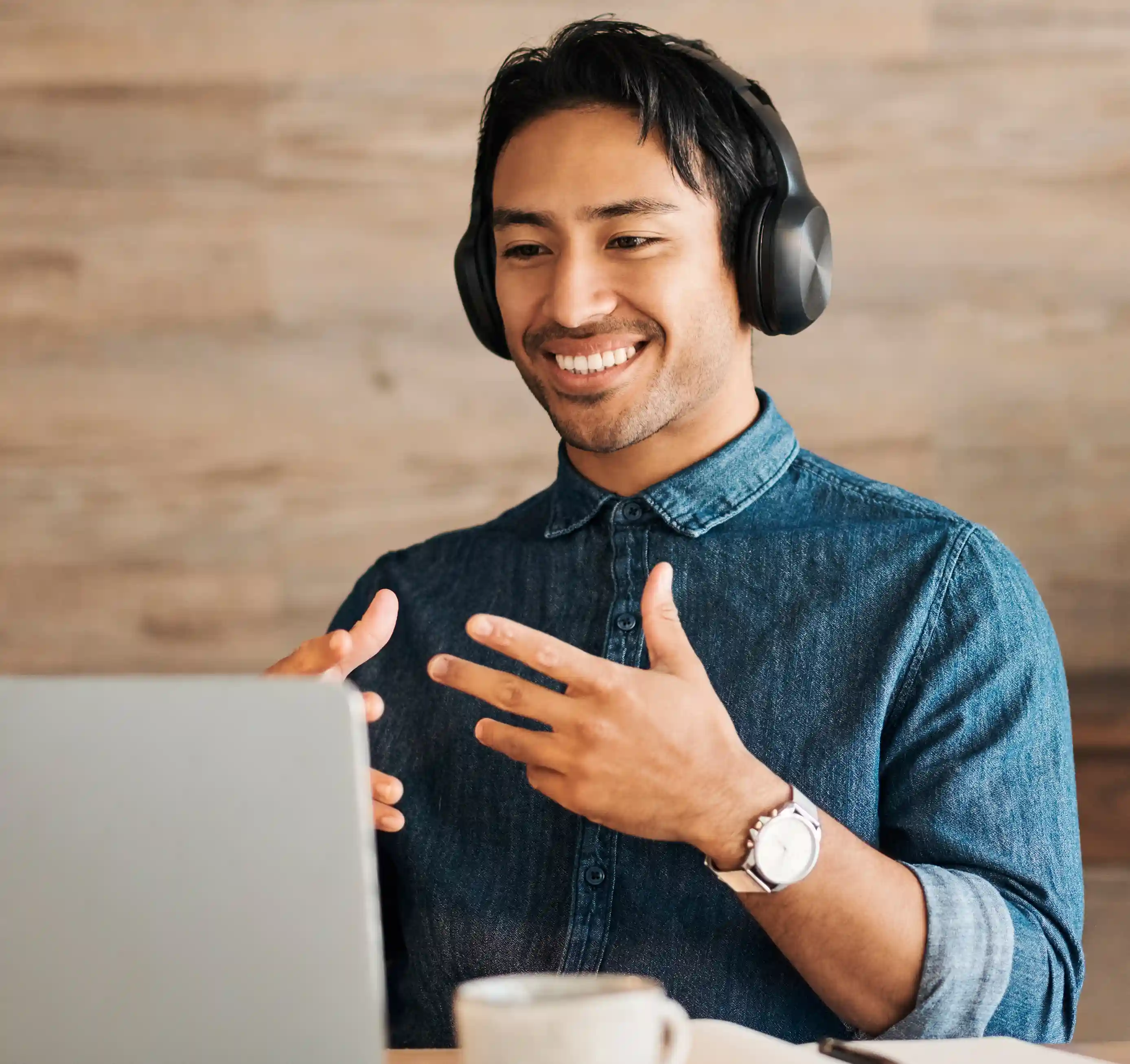 Man wearing headphones and a denim button down is smiling and looking at his laptop screen