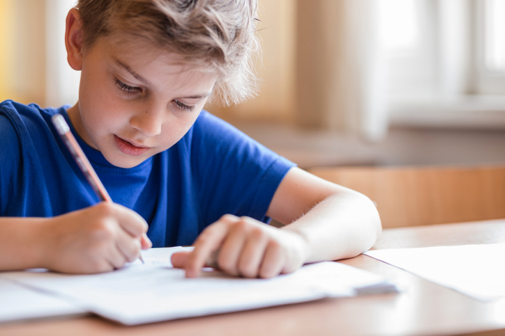 A young boy writing in a classroom setting, representing possible dysgraphia and writing disorders.