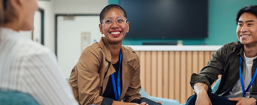 Three healthcare workers conversing and smiling while sitting in blue chairs.